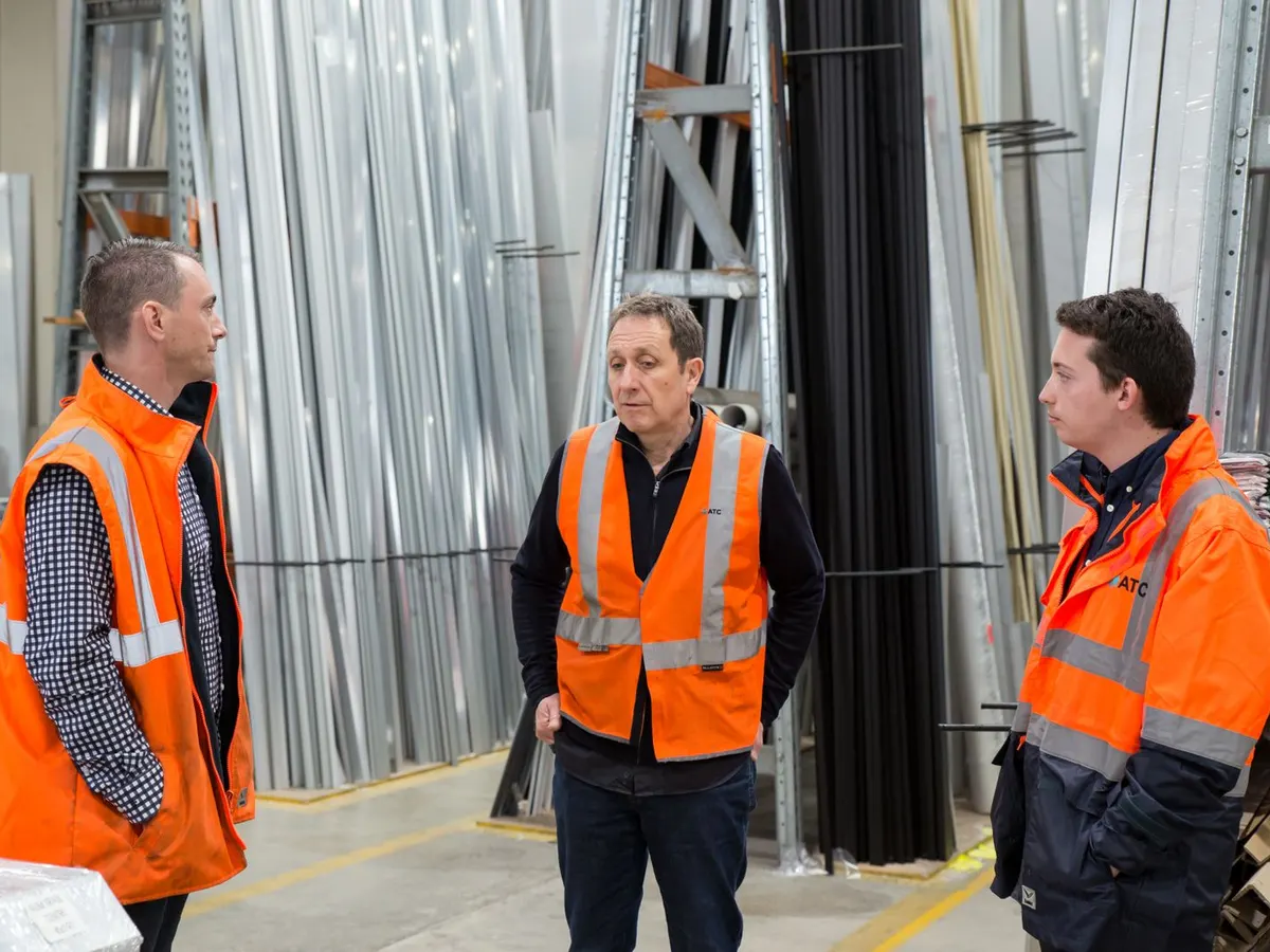 Three colleagues in high-visibility clothing discussing work inside a warehouse.