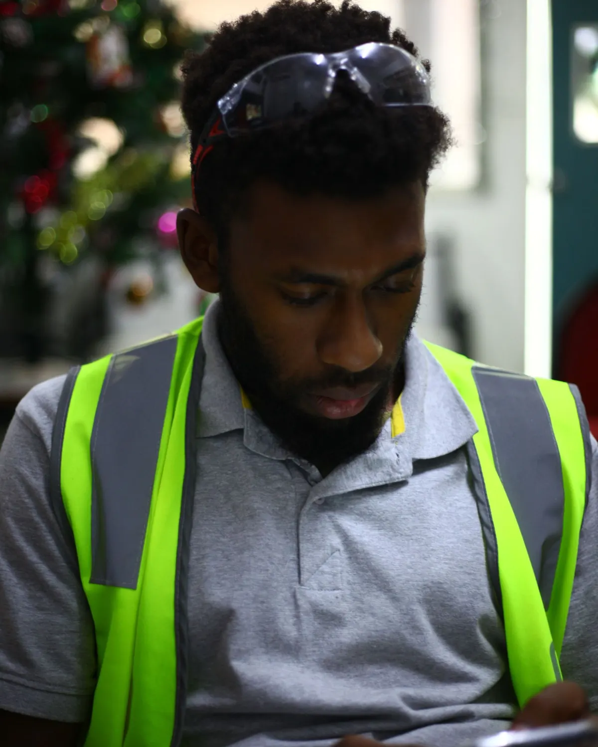 A stationary worker in a high-visibility vest checking a handheld phone indoors.